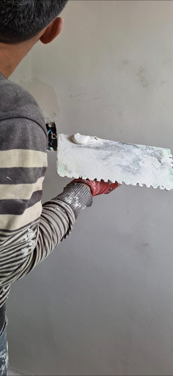 Pintor profesional aplicando enduído plástico con llana para alisar e igualar pared interior
