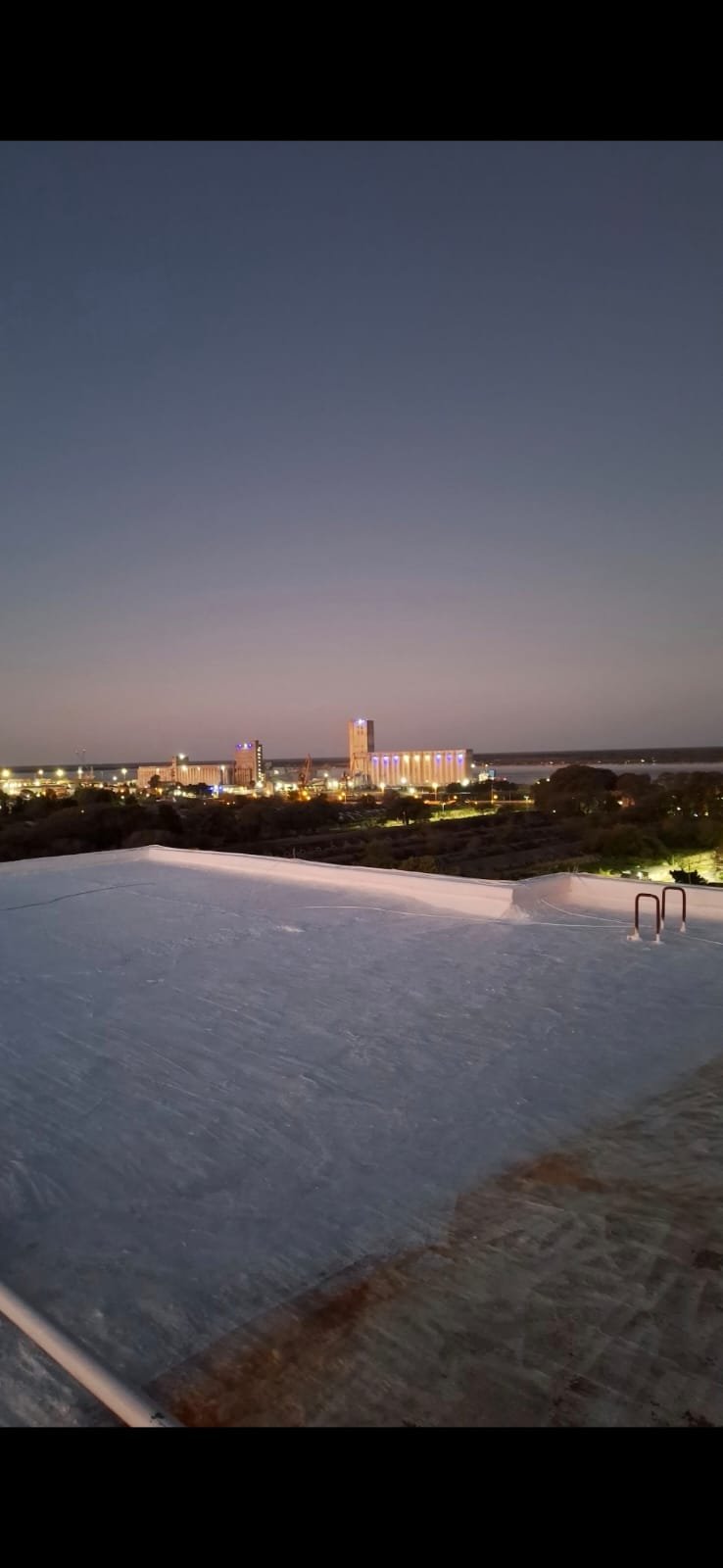 Trabajo terminado de impermeabilización con membrana líquida blanca en terraza de edificio frente al río